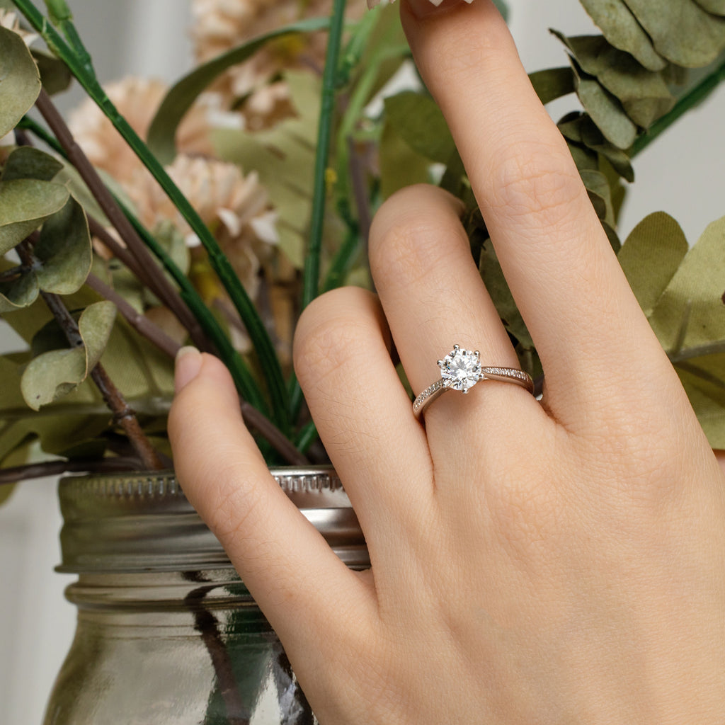 Hand wearing a diamond ring with a blurred background of greenery